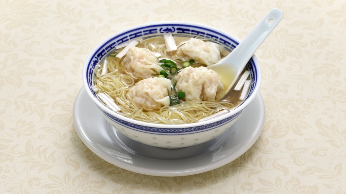 a white and blue bowl with a white soup spoon filled with a favorite hing kong food dumplings mixed with thin rice noodles