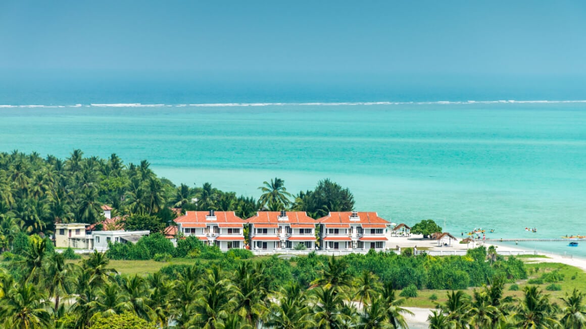 white beach resort with an orange roof surrounded by palm trees and turquoise water