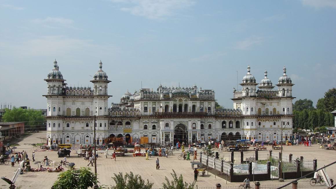 Janaki Mandir Janakpur palace with a white facade and blue windows and people walking around it.