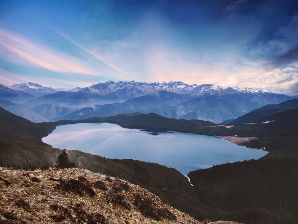 A person sitting on a cliff gazing at the sunset over Rara lake in Rara National Park in Nepal 