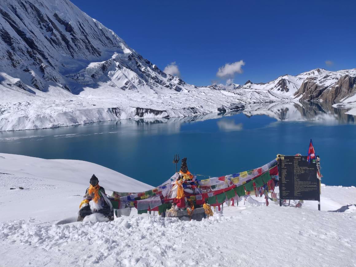 sky blue high altitude lake surrounded by snow covered mountains and a matching blue sky