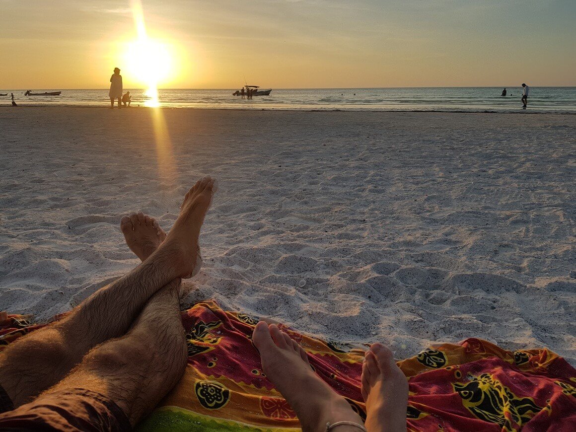 Two pairs of legs crossed over relaxing on a blanket watching the sunset at the beach