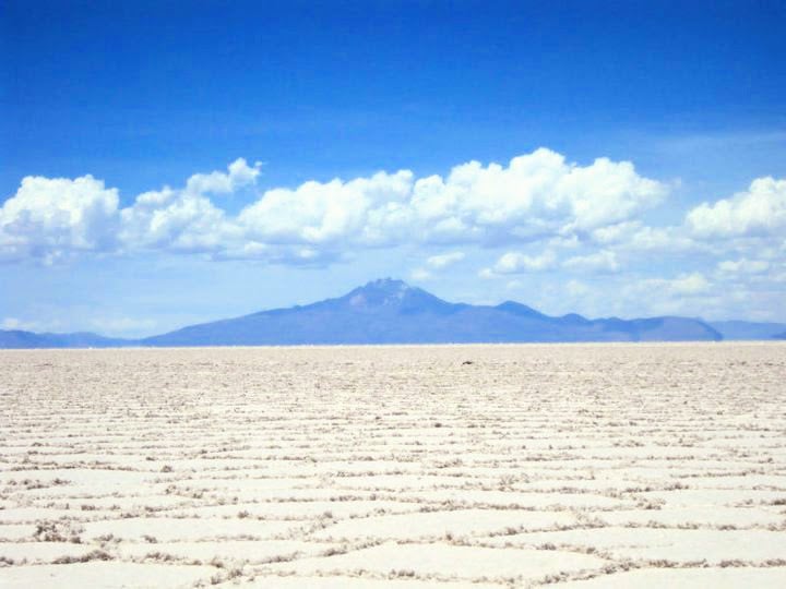 Uyuni salt flat view with mountain behind and blue sky.