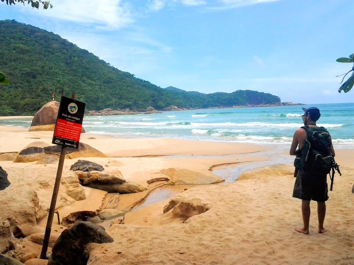 Backpacker arriving to hidden beach Antigos in Brazil. 
Green sea and mountains on the back. 