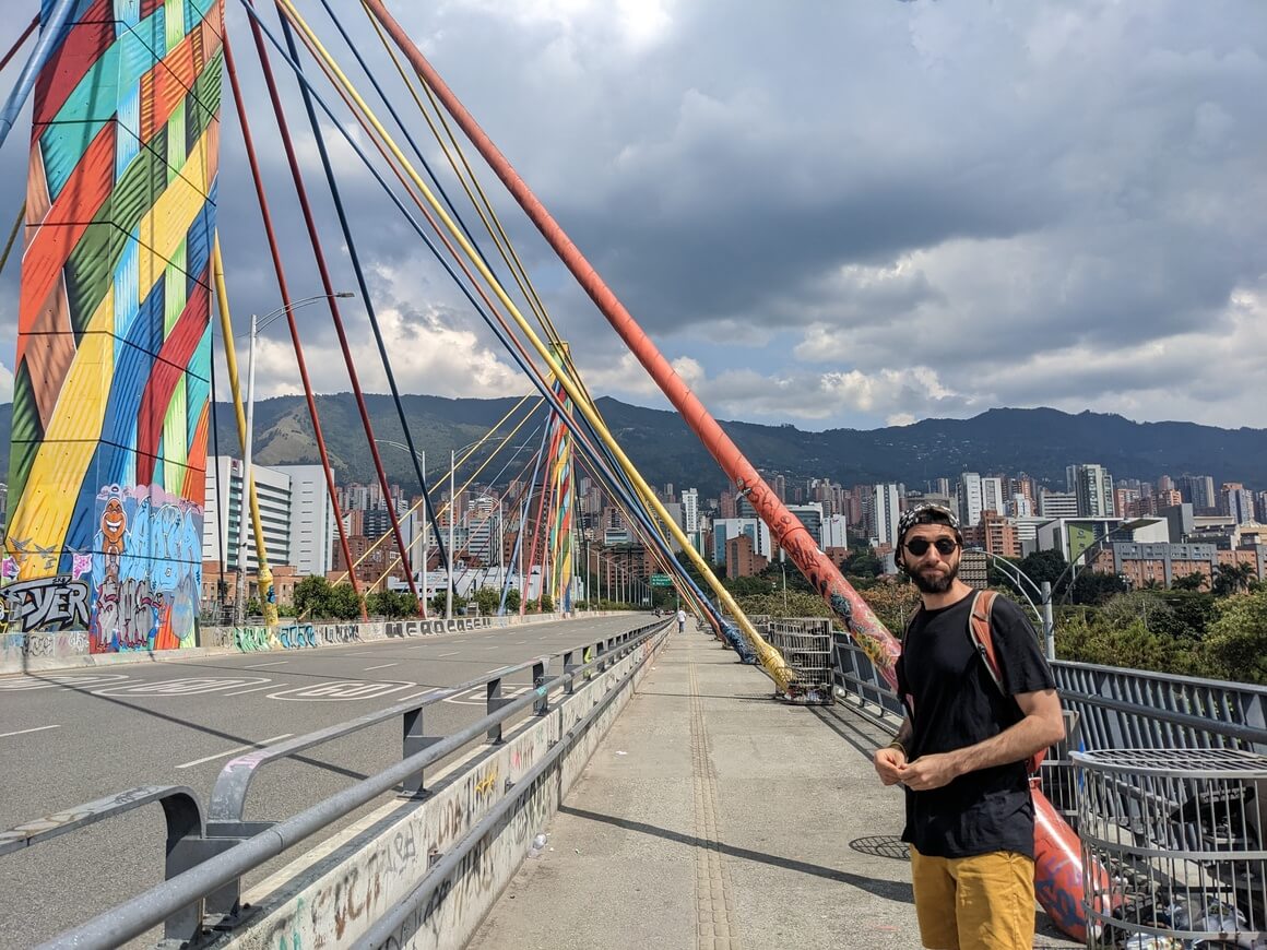 Man with black t-shirt, cap, and sunglasses, on the colourful river bridge in Medellin