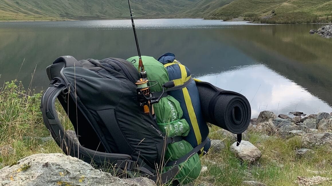 a backpack, tent and fishing rod by a lake
