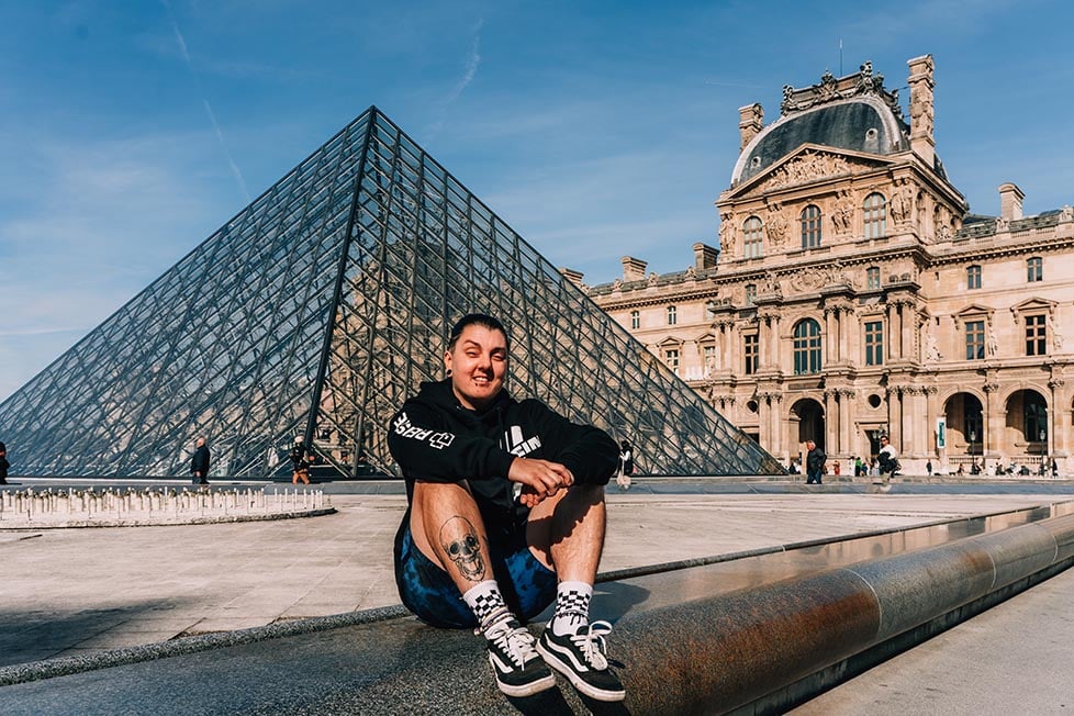 A person sat by the fountains at The Louvre with the pyramid in the background in Paris, France