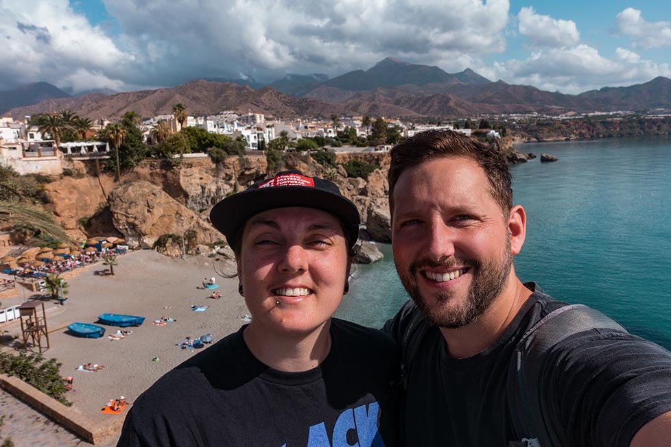 Two people doing a selfie in front of a rugged coastline and beach