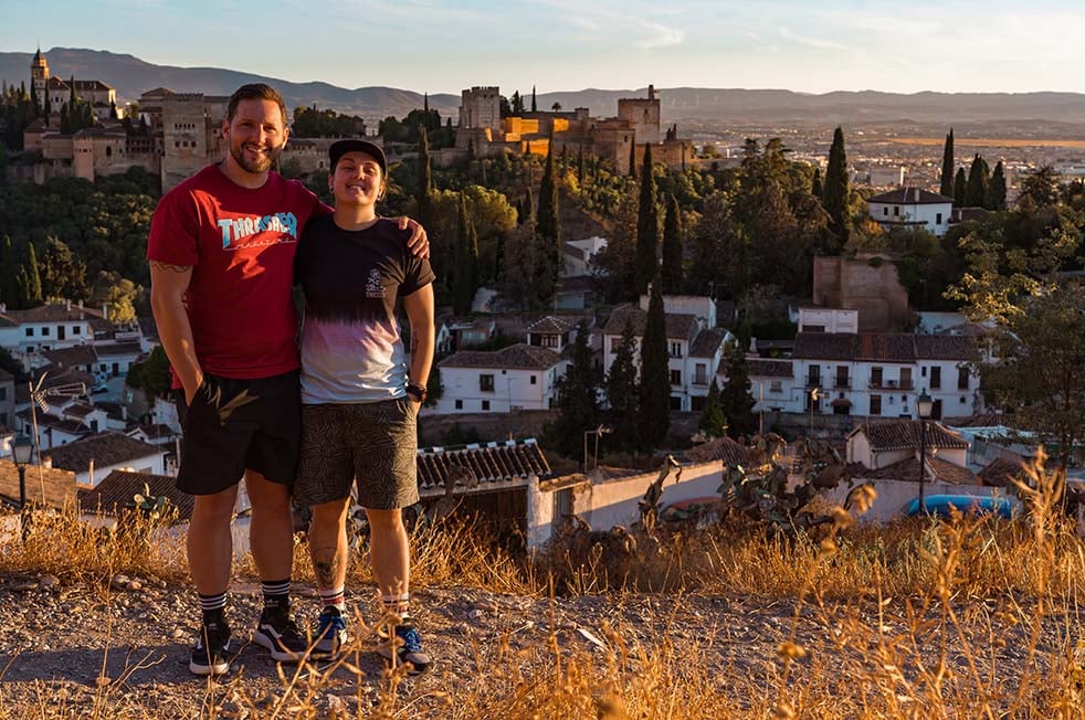 Two people stand in front of Alhambra at sunset