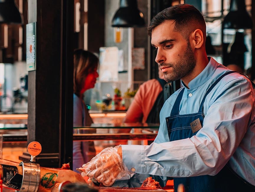 A man in a market in Spain carves Jambon.