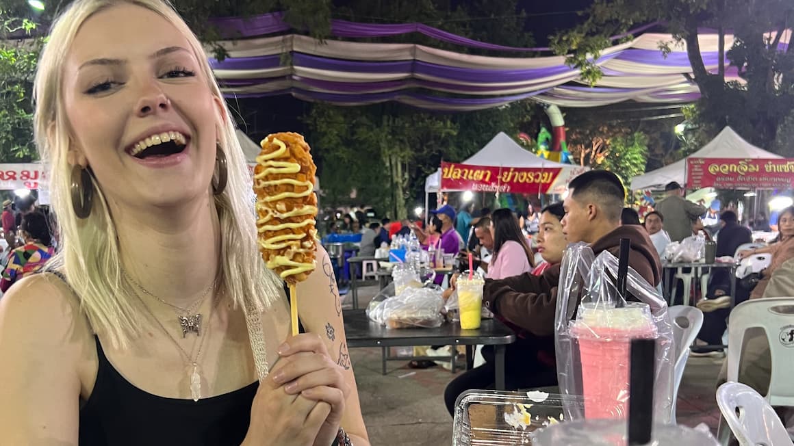 a girl eating a corn dog at a market in thailand