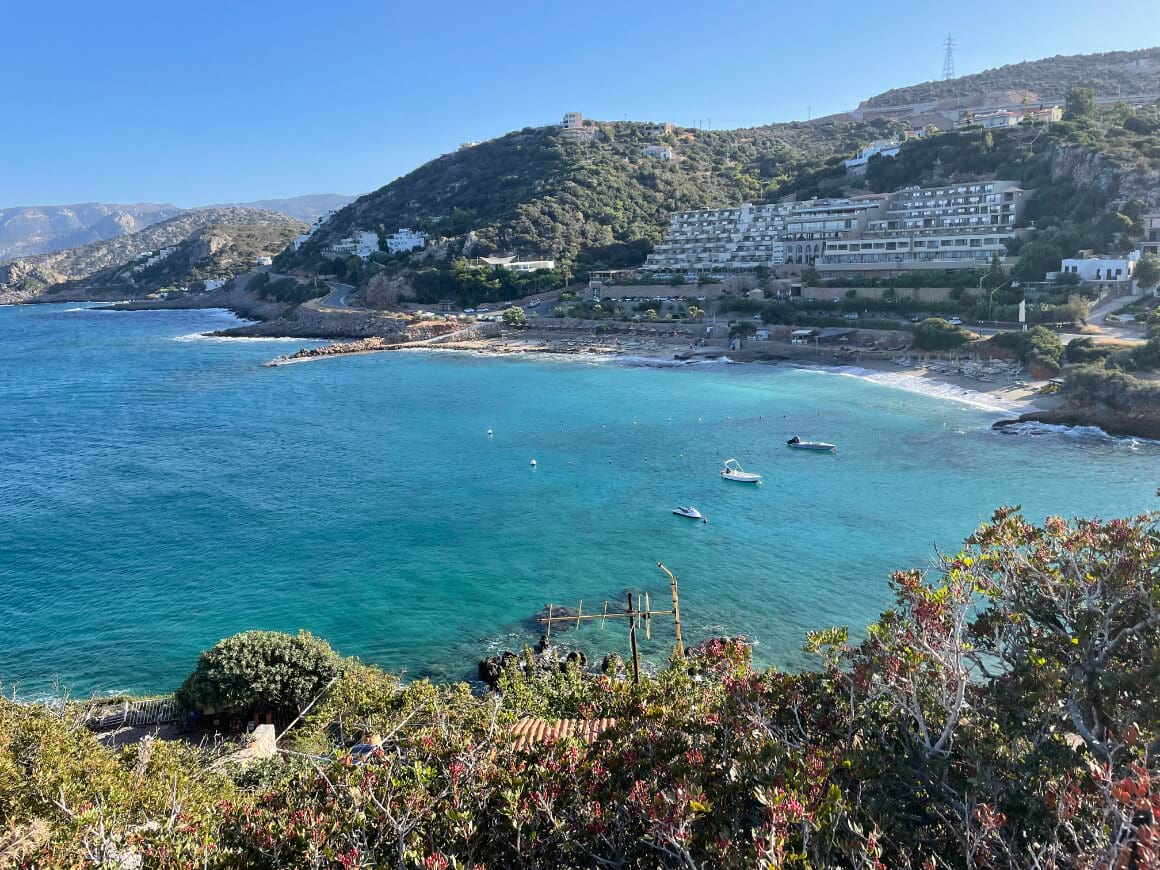 A view of a beach with boats in the water and a hotel in the background in Crete Greece