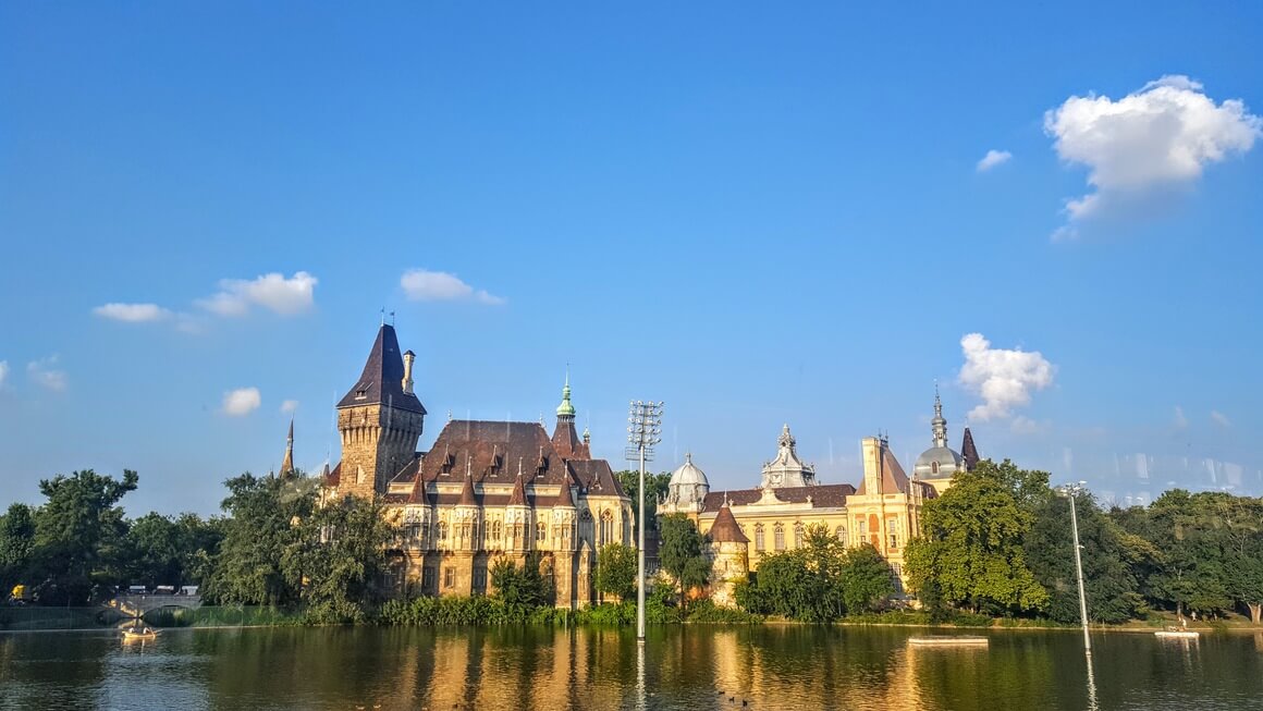 Traditional Hungarian building with a tower reflecting on lake.