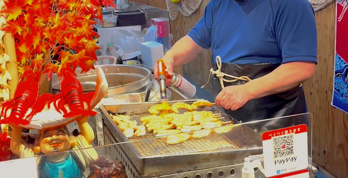 A man cooks shrimp at street food stall in market in Kyoto, Japan.