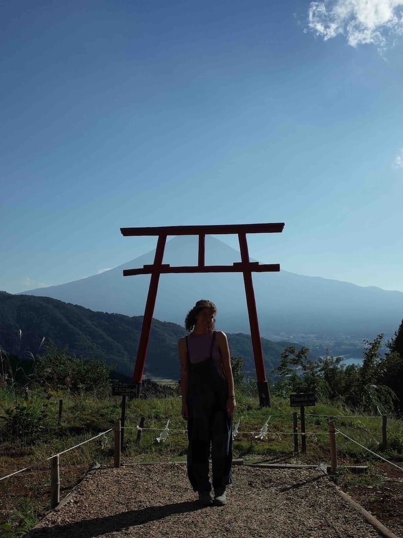 Girl poses for photo under shrine overlooking views of fuji-san.