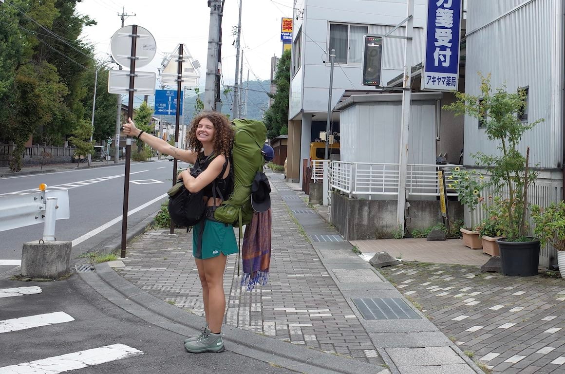 A girl smiling and hitchhiking through Japan.