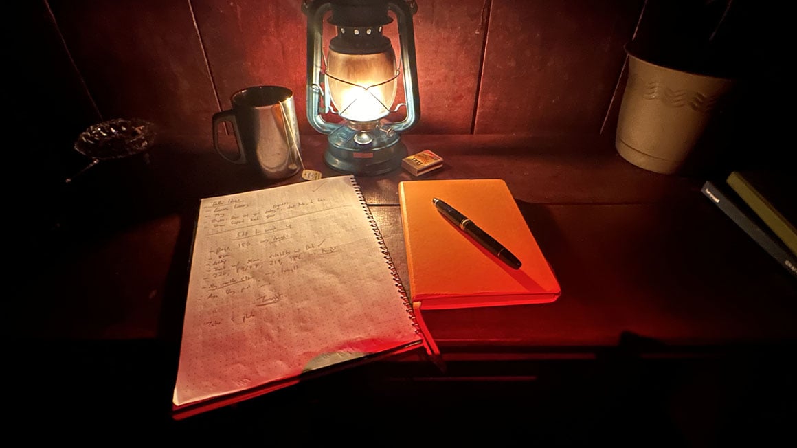Kerosene lamp lighting up a journal with a pen and a note pad at nighttime.