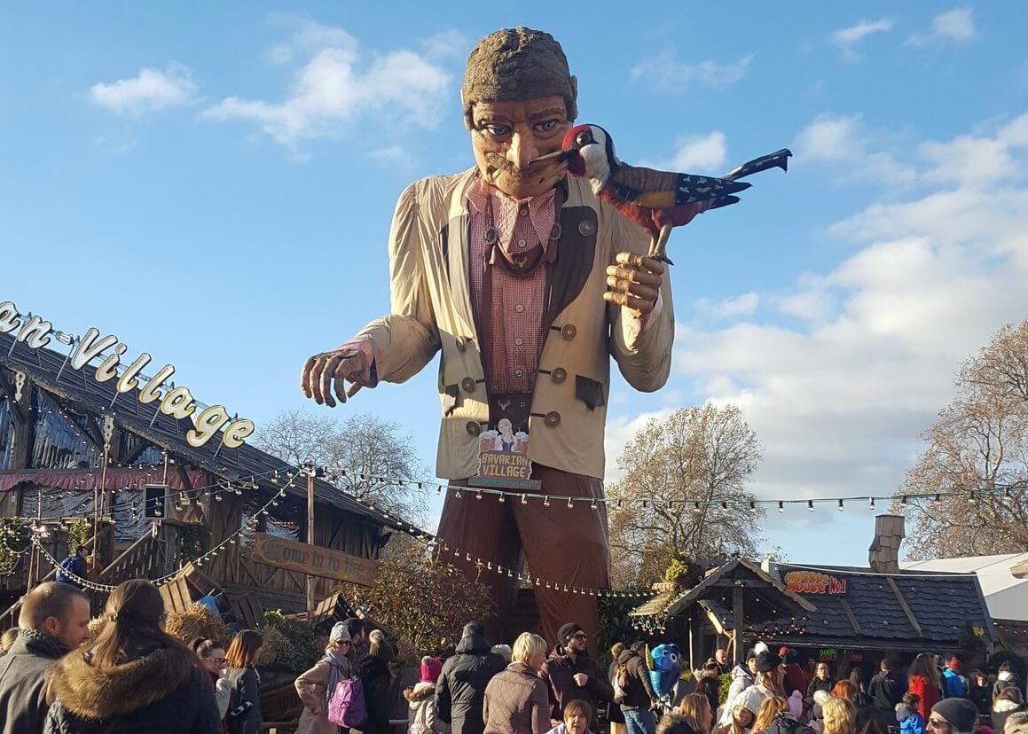Huge wooden state of a man holding a bird overlooking busy christmas markets 
