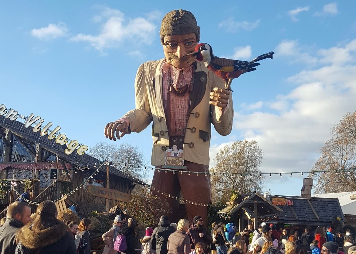 Huge wooden state of a man holding a bird overlooking busy christmas markets