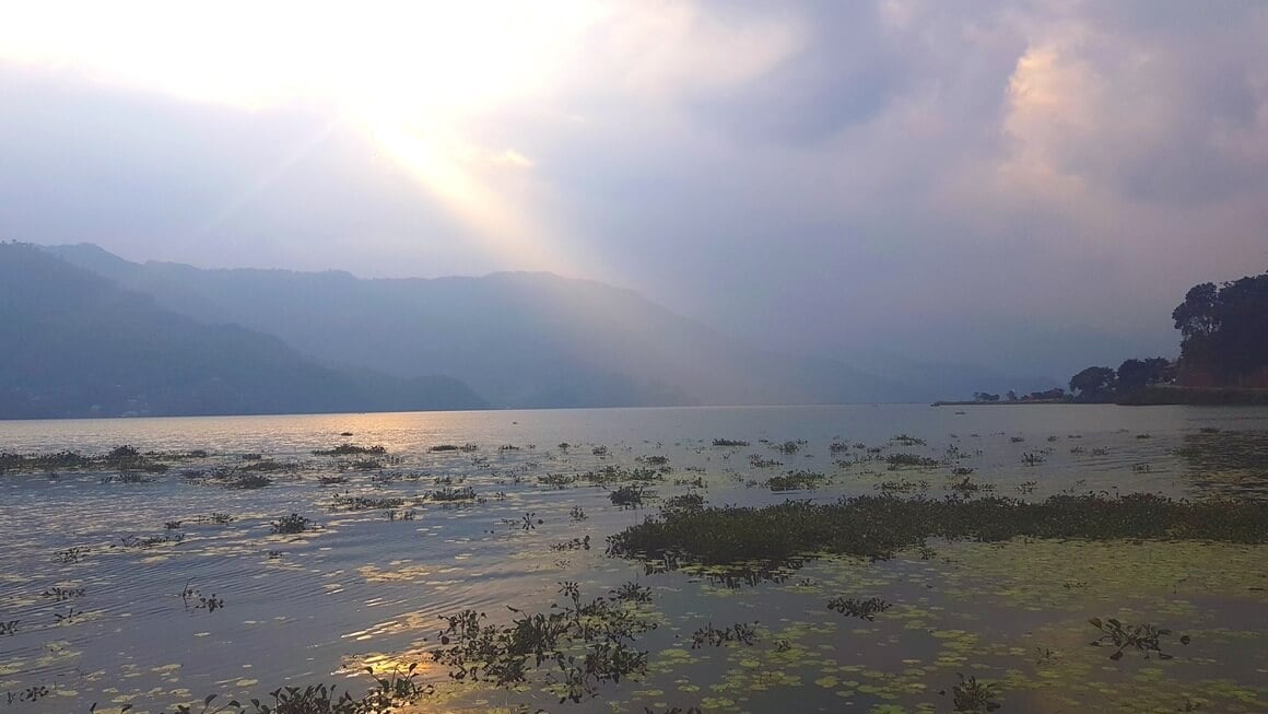 Phewa Lake in Pokhara, Nepal on a cloudy day with sunrays breaking through the clouds.