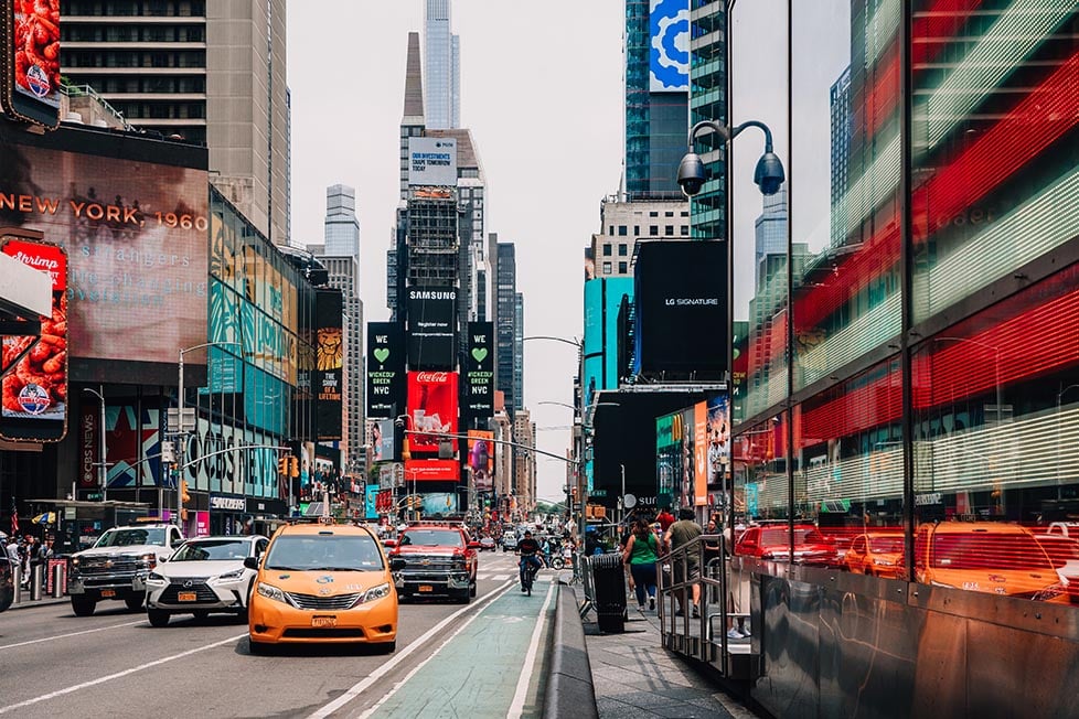 A yellow taxi and USA flag with Times Square behind