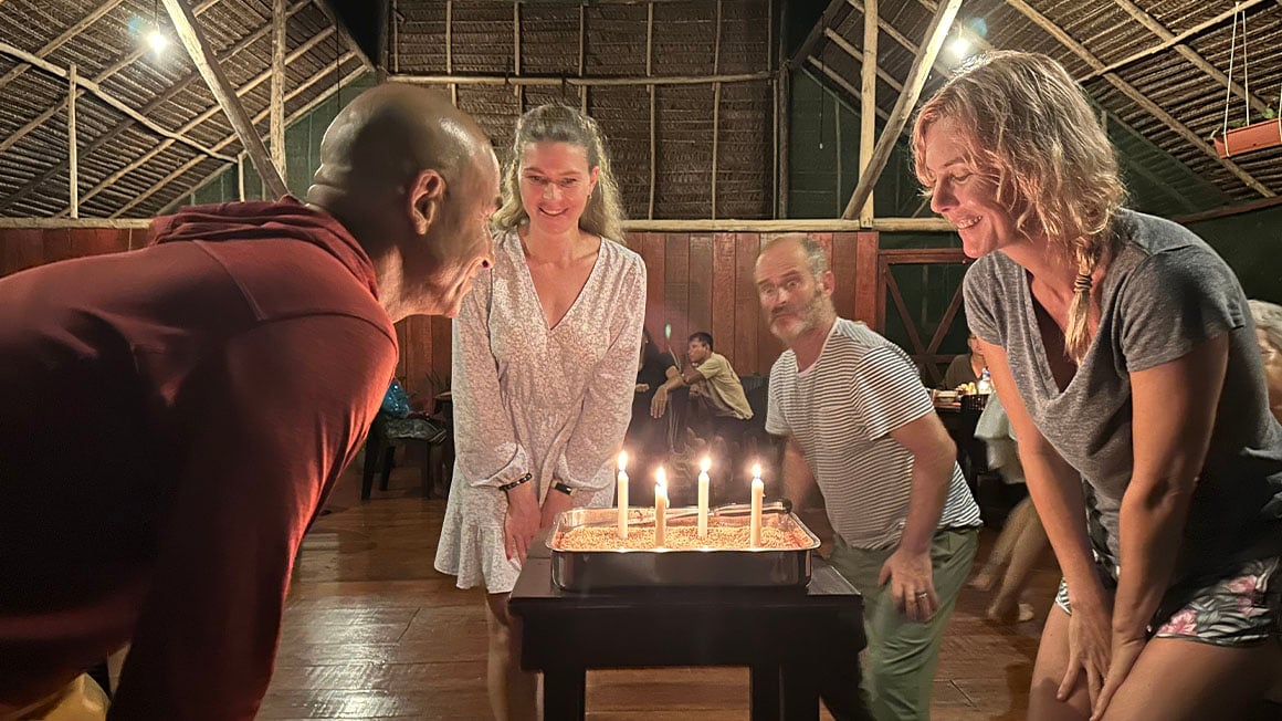 Four people stood around a birthday cake with four lit candles.