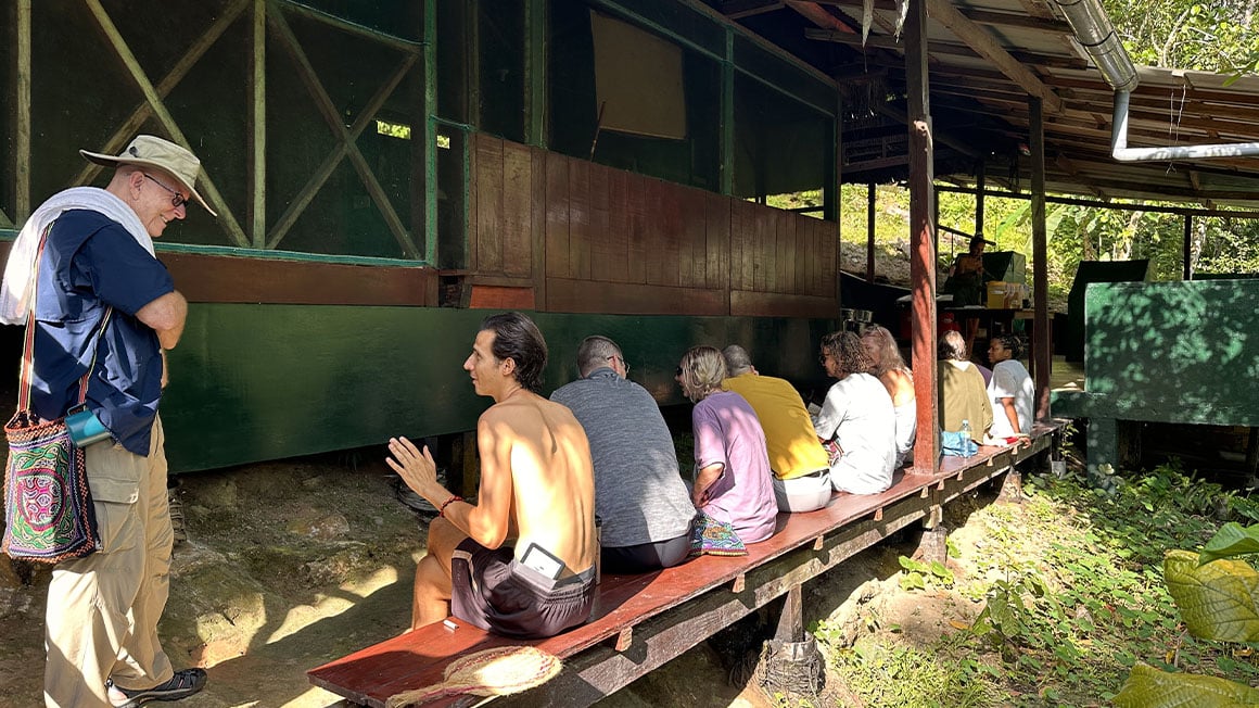 People chatting on a bench and stood up in the shade.