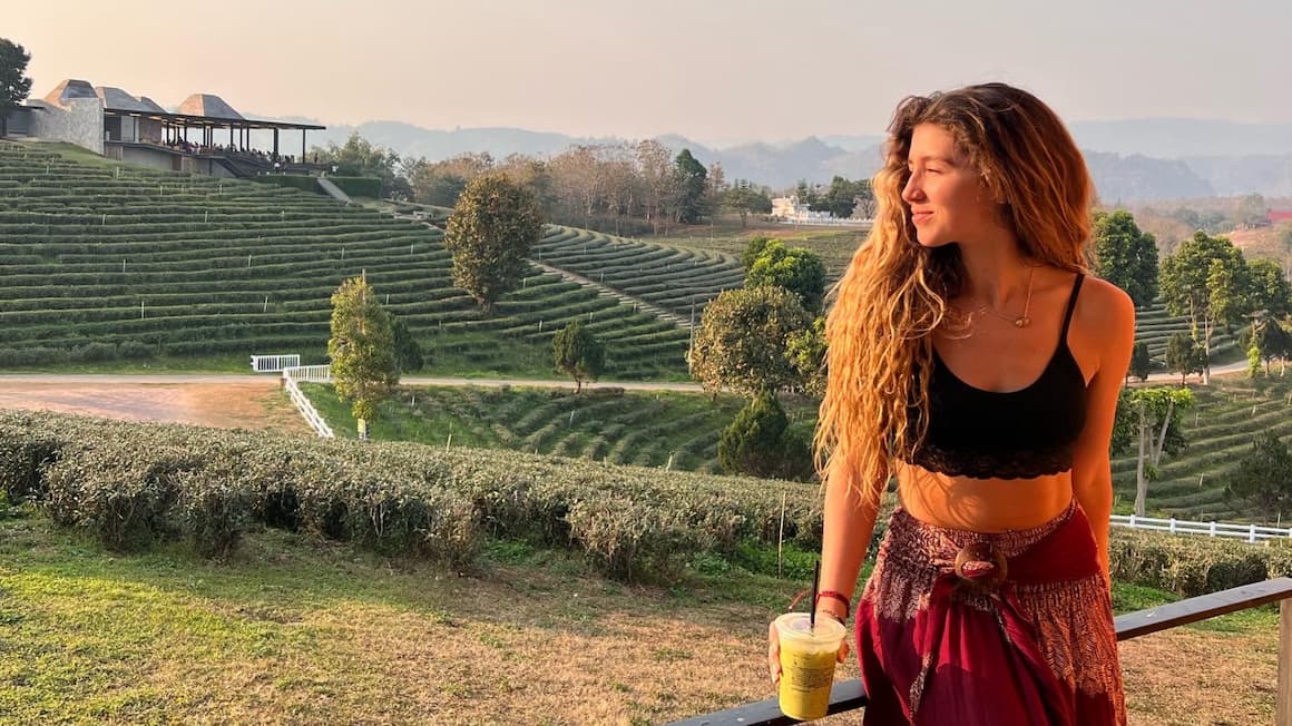 a girl smiling with an iced green tea in her hand, looking at the sunset