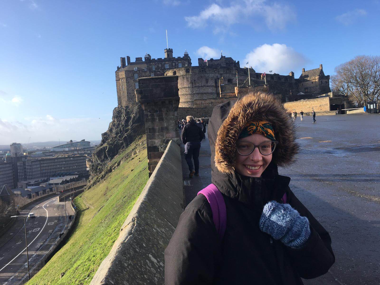 woman wearing a big winter coat and thick gloves outside Edinburgh Castle on a sunny day