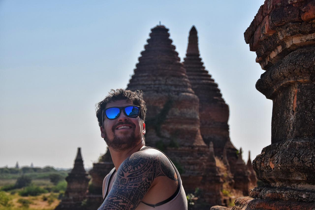 man wearing blue sunglasses smiling while being surrounded by ancient temples in bagan myanmar