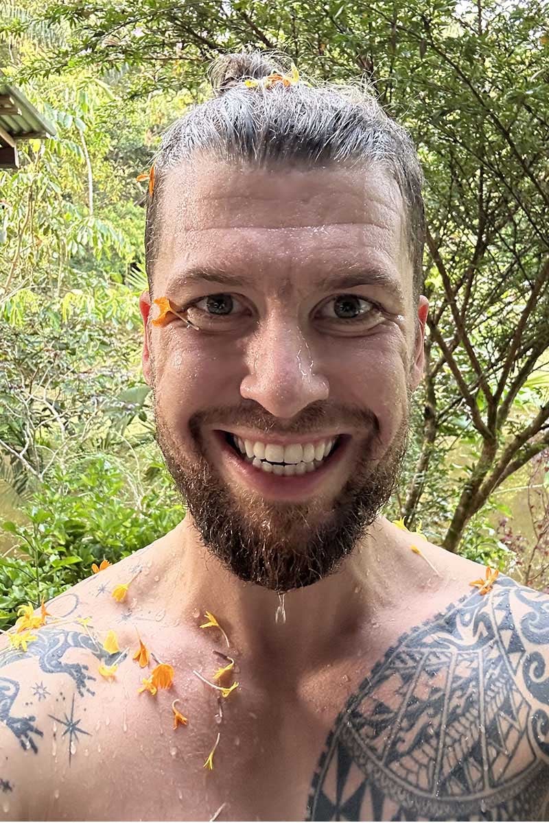 Tattooed man smiling after a flower bath in ayahuasca retreat.