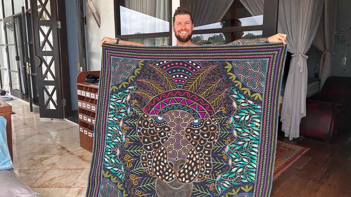 Man holding up a tapestry with full arm span of a mandala style print of a jaguar