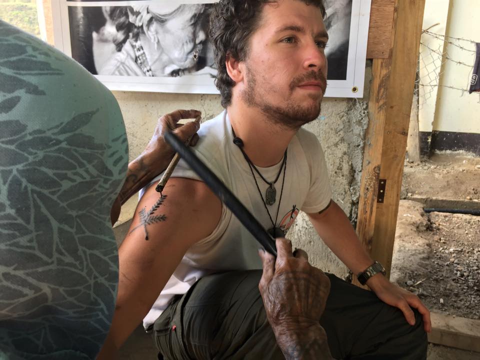 man in a white shirt sitting and getting tattooed by legend whang od using the  bamboo stick and poke method in the philippines
