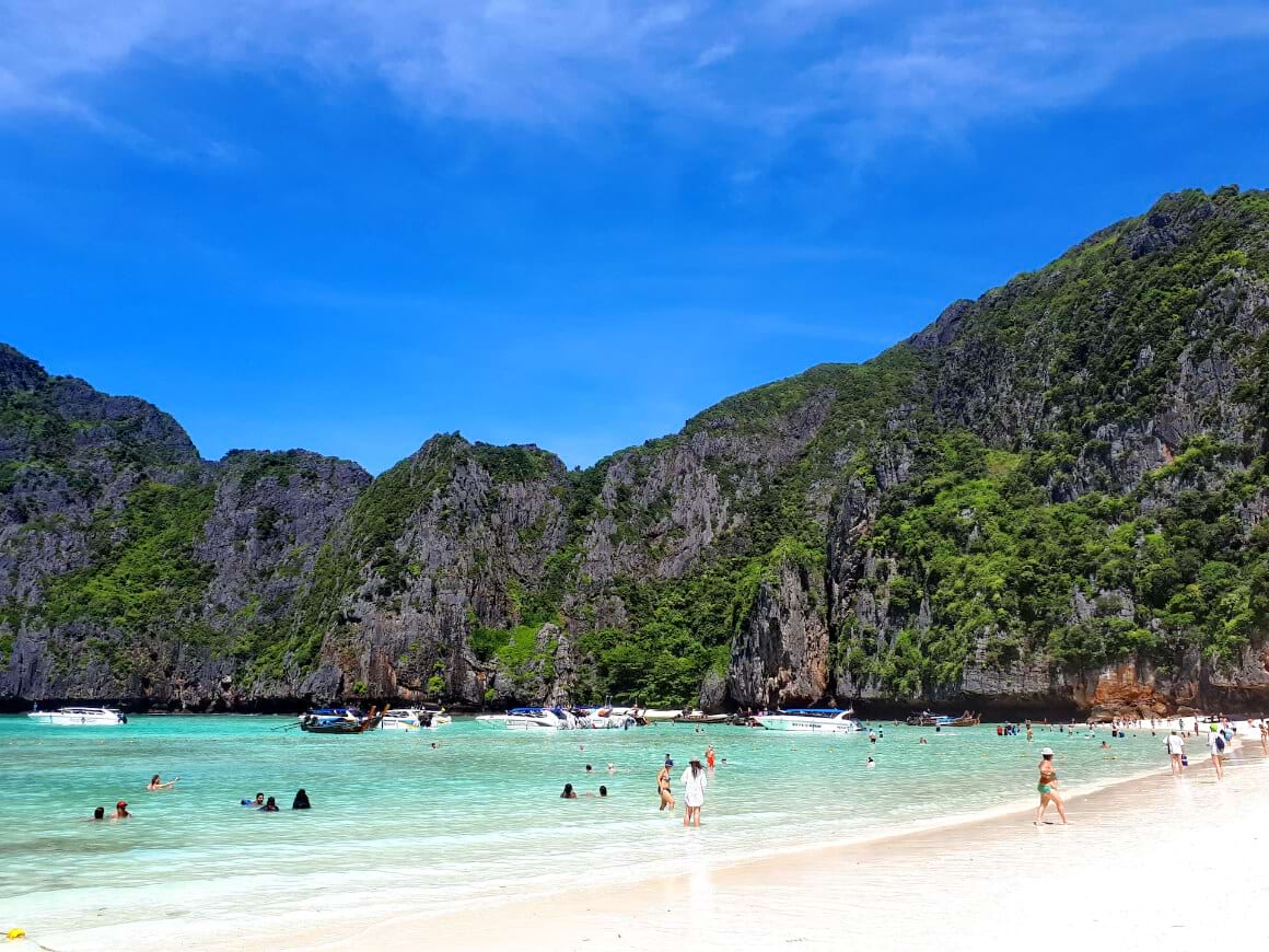 A group of people swimming in the turquoise beach of Maya Bay surrounded by mountains