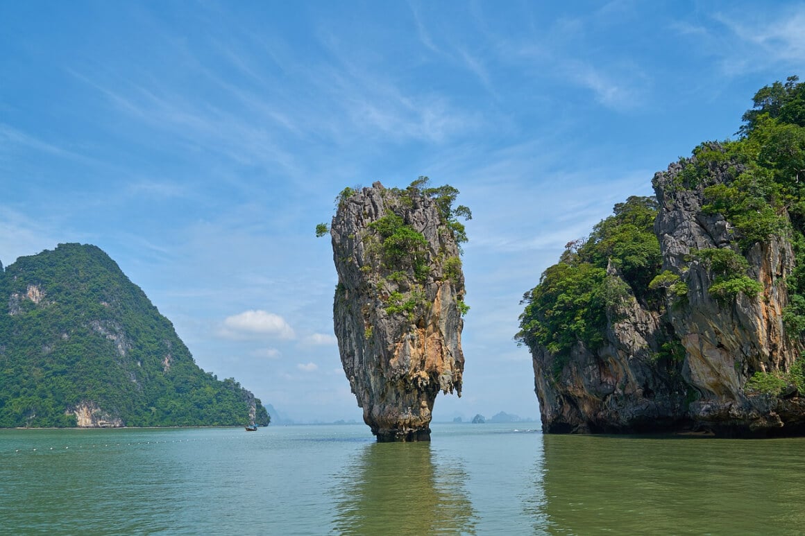 A rock formation standing high in the middle of emerald-green water in Phang Nga Bay surrounded with other rocky formations 