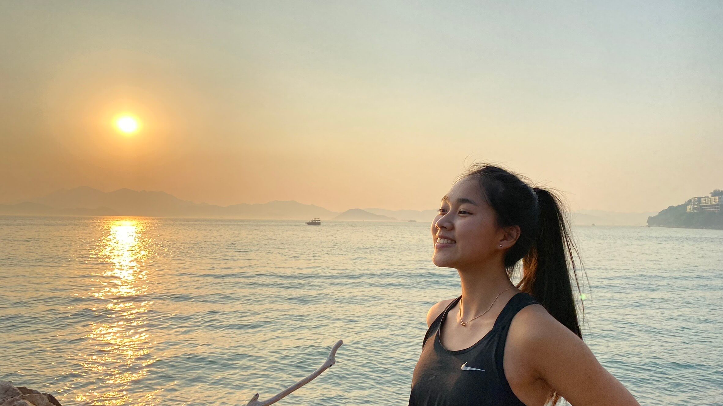 girl standing in front of water at sun set while traveling and eating in hong kong