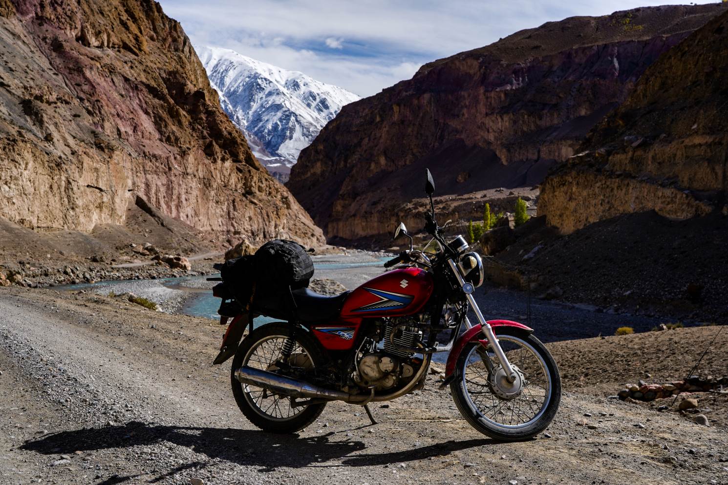 red motorbike in front of bright blue river and mountains in hunza valley pakistan