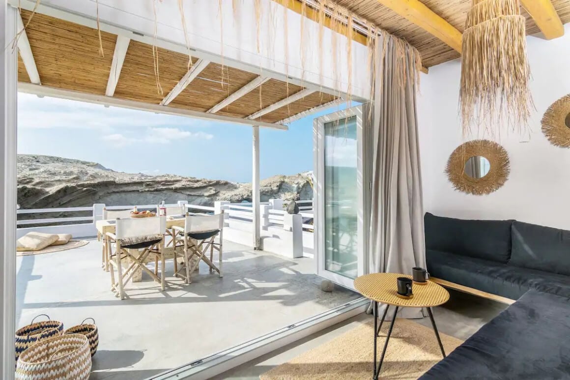 View from inside the house and onto the large white terrace with a table set on it. Bohemian chic style decor. View of the rocks can be seen behind the terrace.