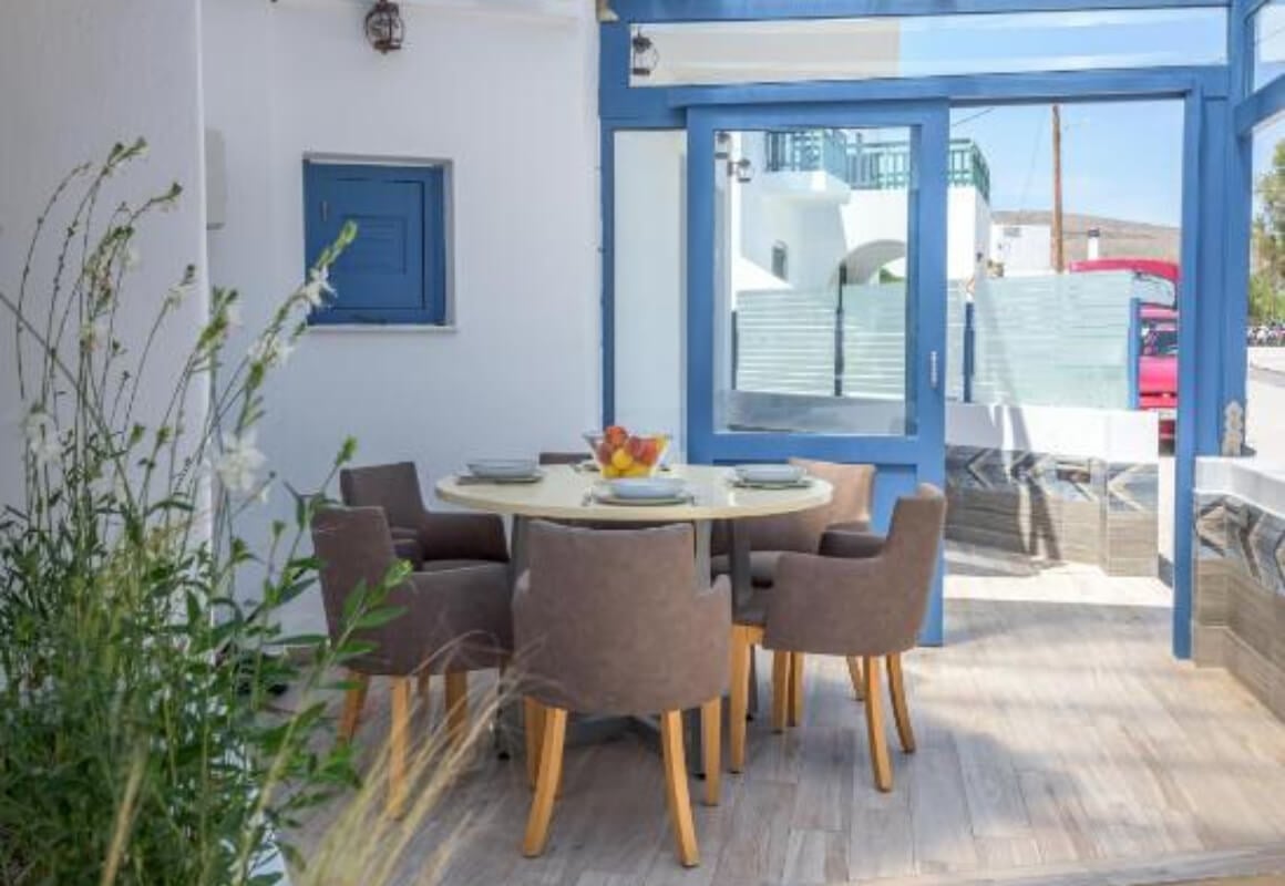 Blue and white, light coloured patio area with a round table set for 4 in the centre.