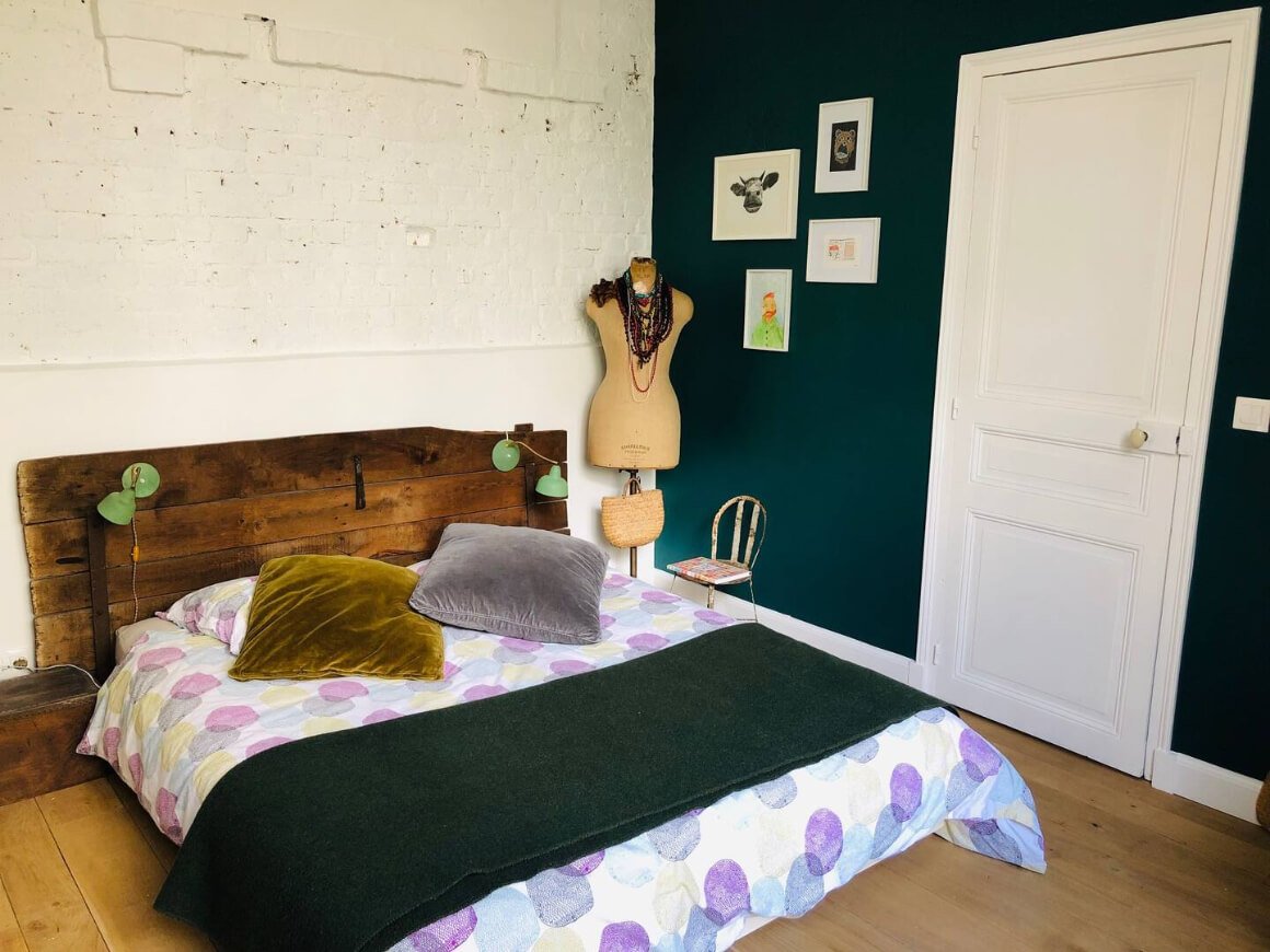 Bedroom with a rustic vibe. Dark green wall and blanket with a wooden head board.