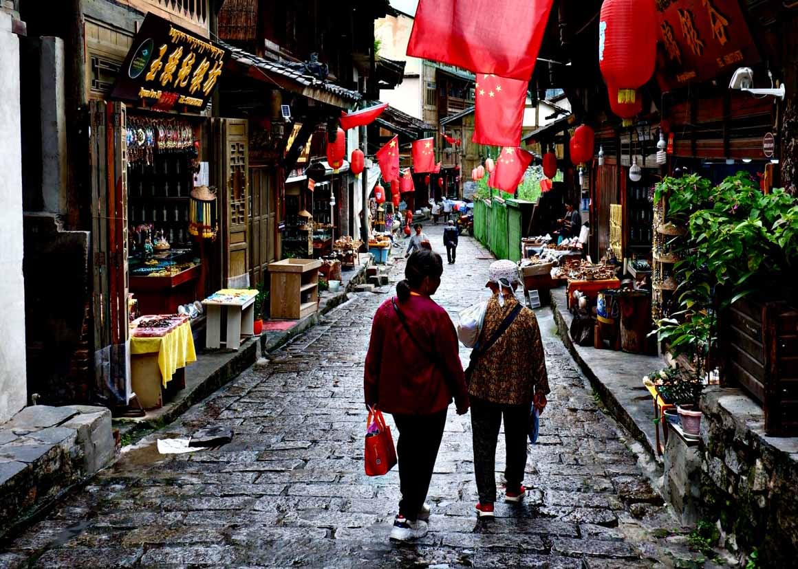 Two old ladies walking down a traditional street lined with Chinese flags