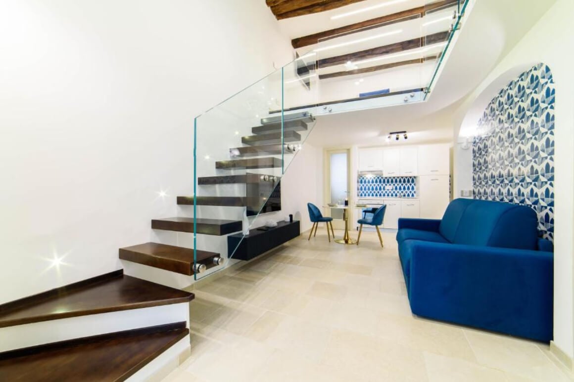 Luxury living area with blue couch and dining chairs. Modern staircase to get up to second floor.