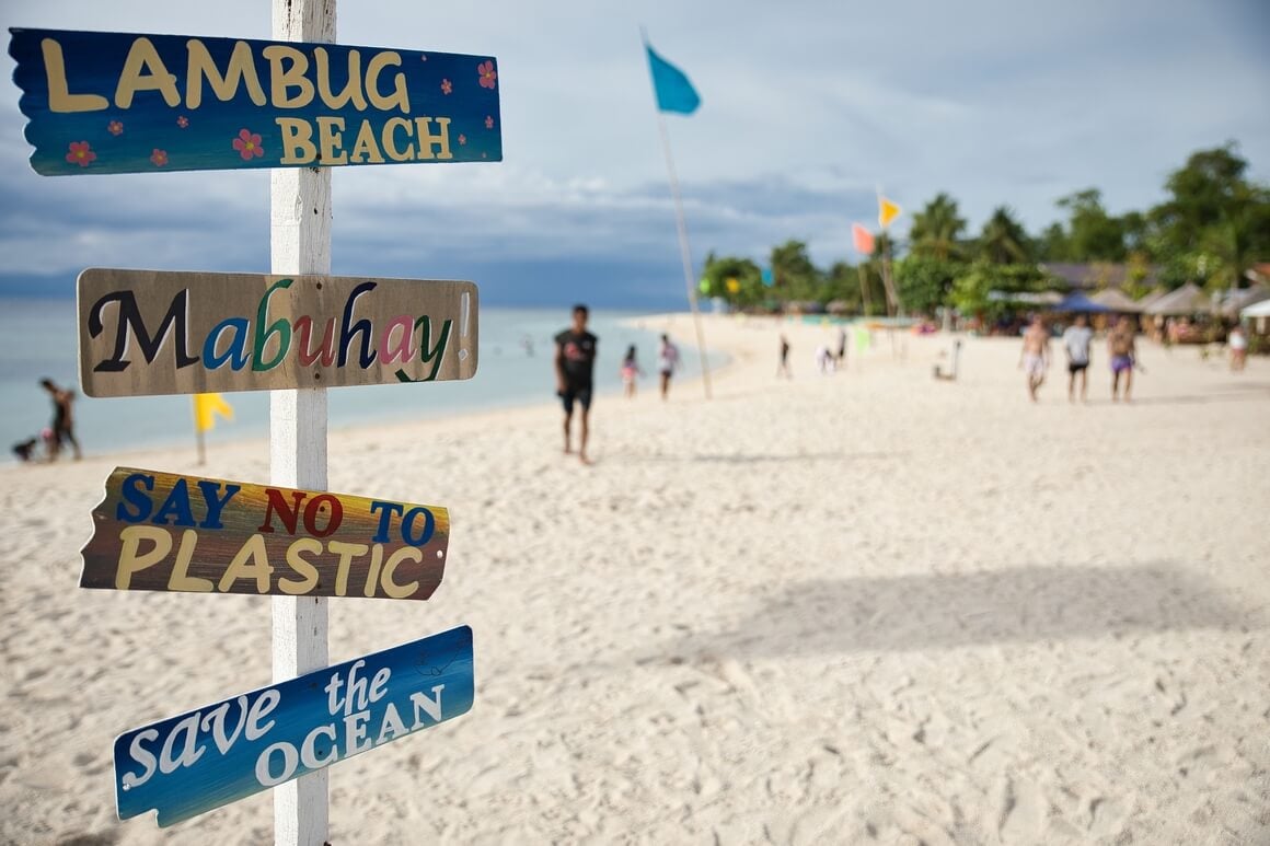 Dream beach of Moalboal Cebu in the Philippines with palm trees along the beach and a colorful wooden signpost sharp in the foreground.