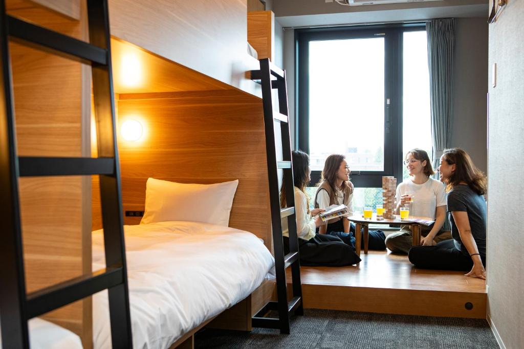 Group of girls sitting in their dorm with a big window behind and a bunk bed at Grids Tokyo Ueno Hotel&Hostel