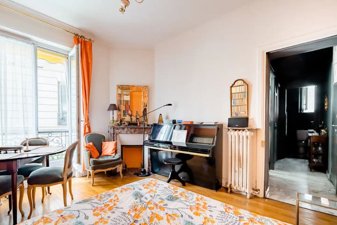 Bedroom with piano, dining table and orange and white colouring. 