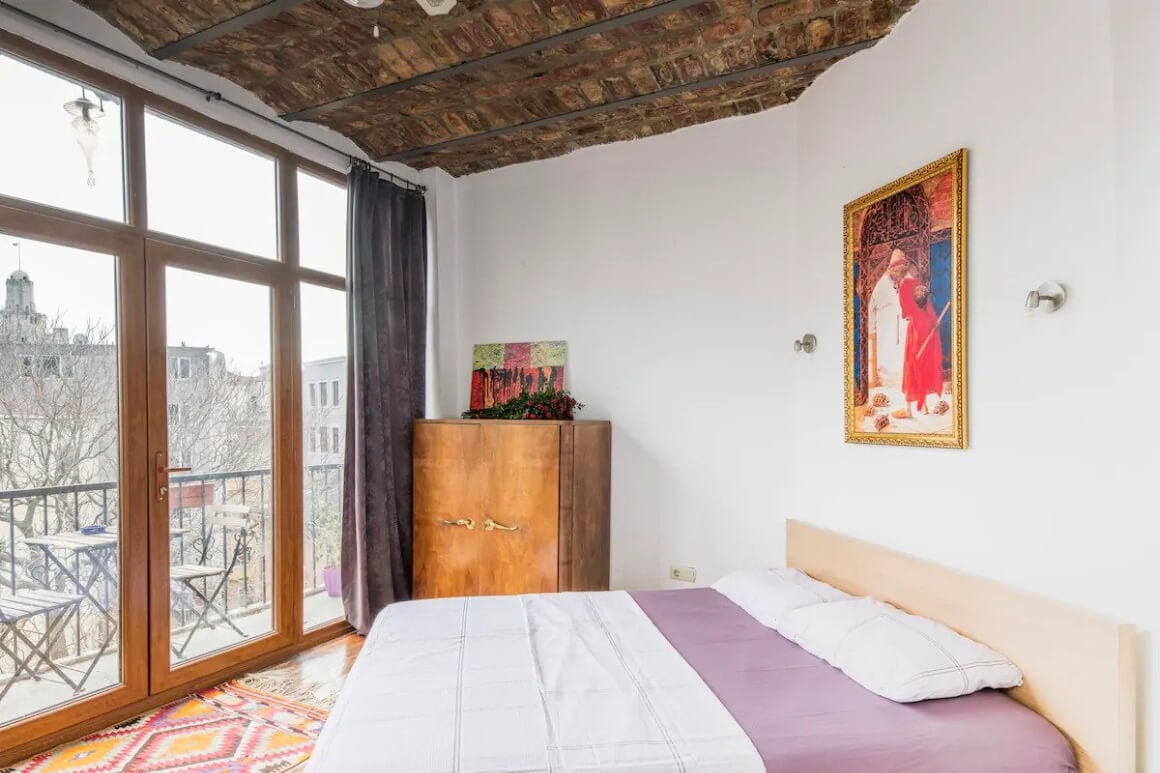 Bedroom with wooden roof and wooden doors that lead out onto small terrace with view over the city.