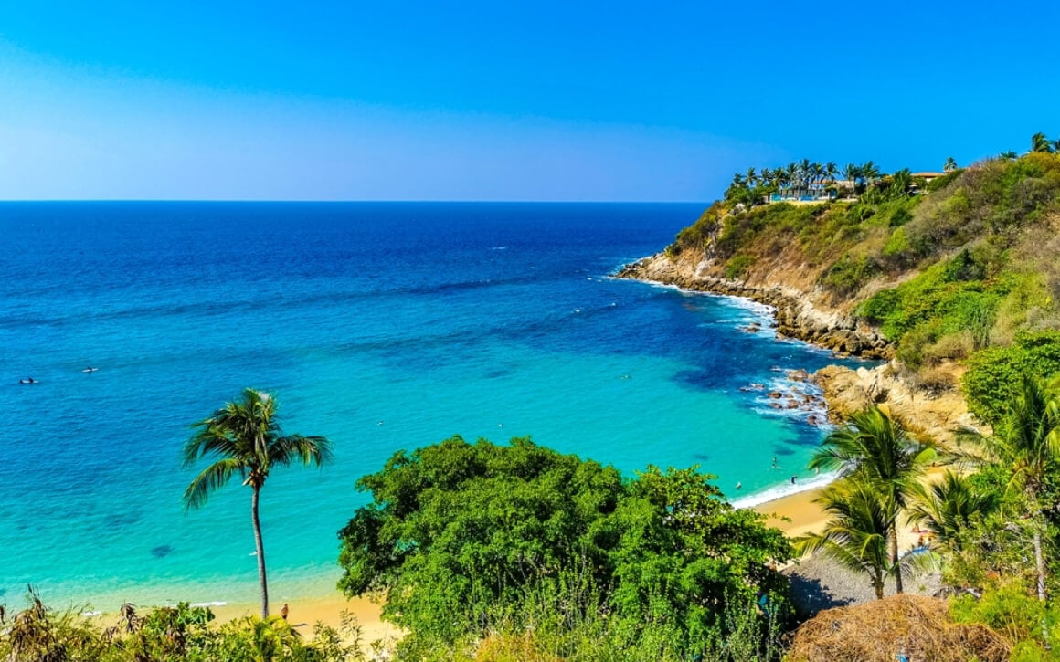Playa Carrizalillo Puerto Escondido surrounded by palm trees and a cliff. 