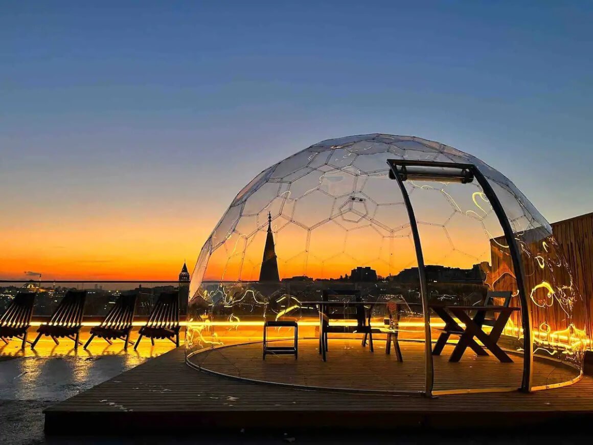 Private rooftop with clear dome with table and chairs inside. Photo was taken at sunset with incredible view of the city in the background