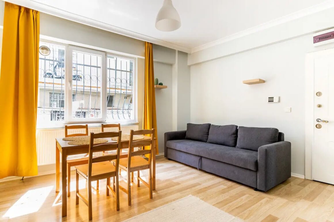 Bright living area with orange curtains, comfy couch and 4-chair dining table