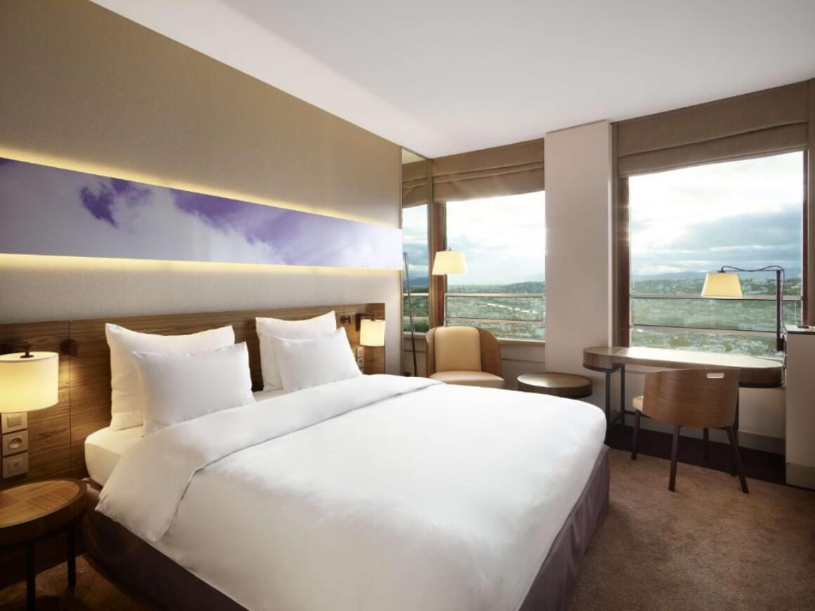 Simple, modern bedroom at Radisson Blu Hotel Lyon. Big windows in the room showing the views over the mountains.